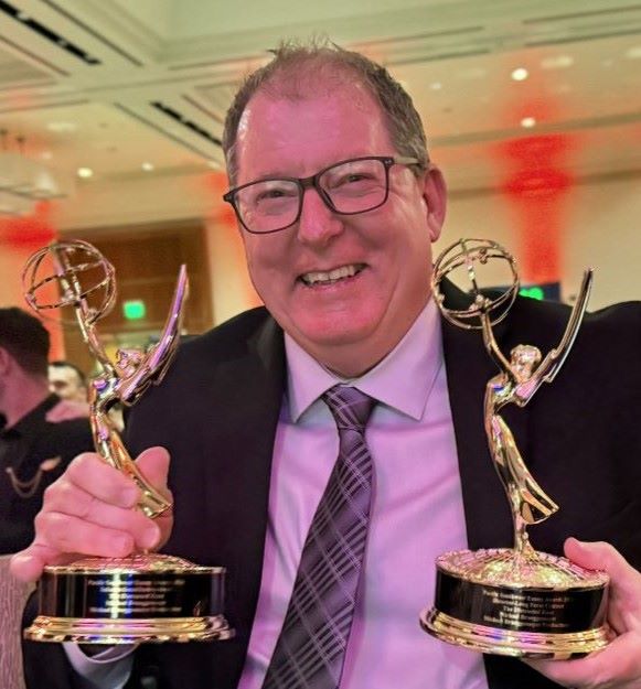 Mike Brueggemeyer smiles while holding Emmys