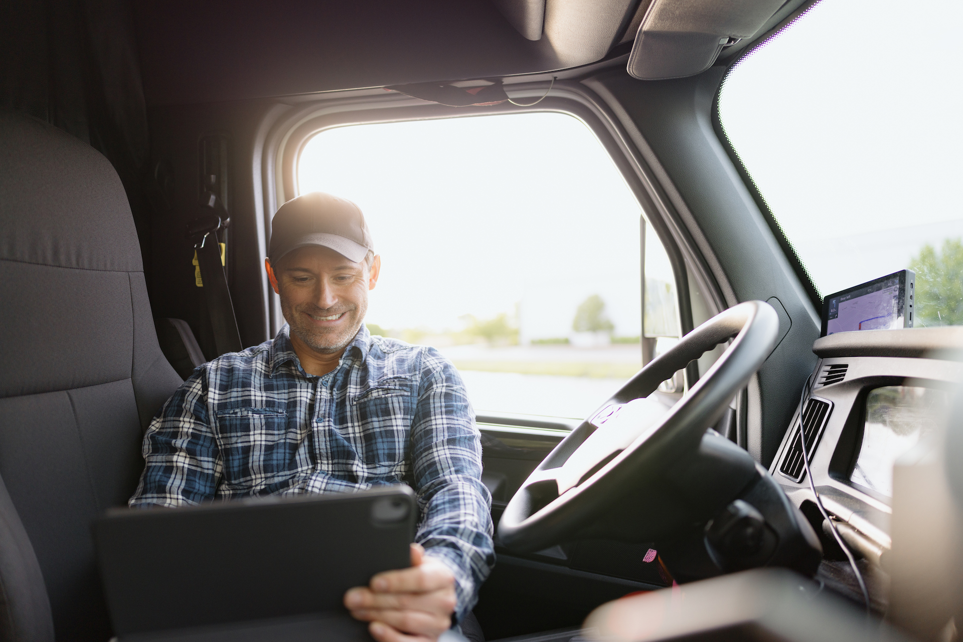 Commercial truck driver sitting in a truck cab and viewing information on a tablet while parked.